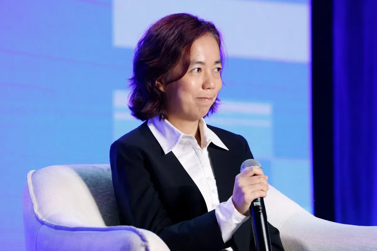 Fei-Fei Li speaking onstage holding a microphone.