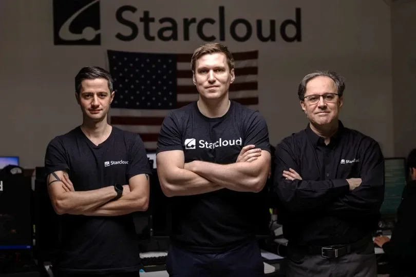 Portrait of Starcloud founders Ezra Feilden, Philip Johnston, and Adi Oltean standing in front of the company logo and an American flag.